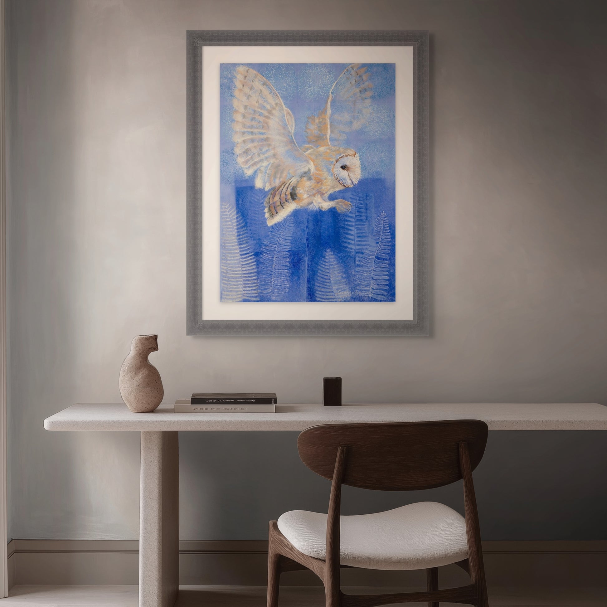 Room mockup of Ethereal Whispers, a framed barn owl painting by Georgia Edwards displayed above a desk in a calm modern interior.